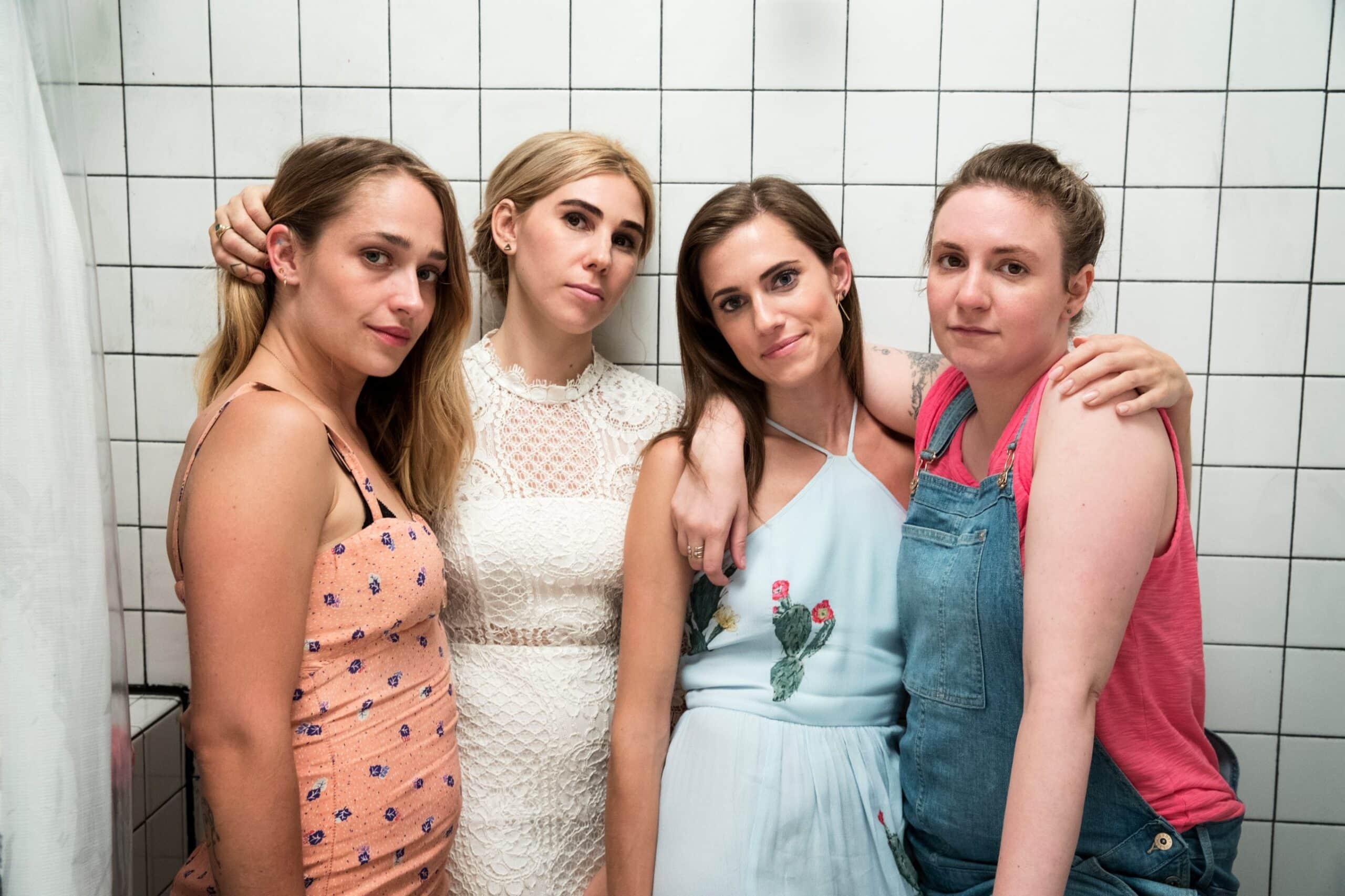 Four women standing arm in arm against a white tiled wall in a promotional still from the HBO series Girls