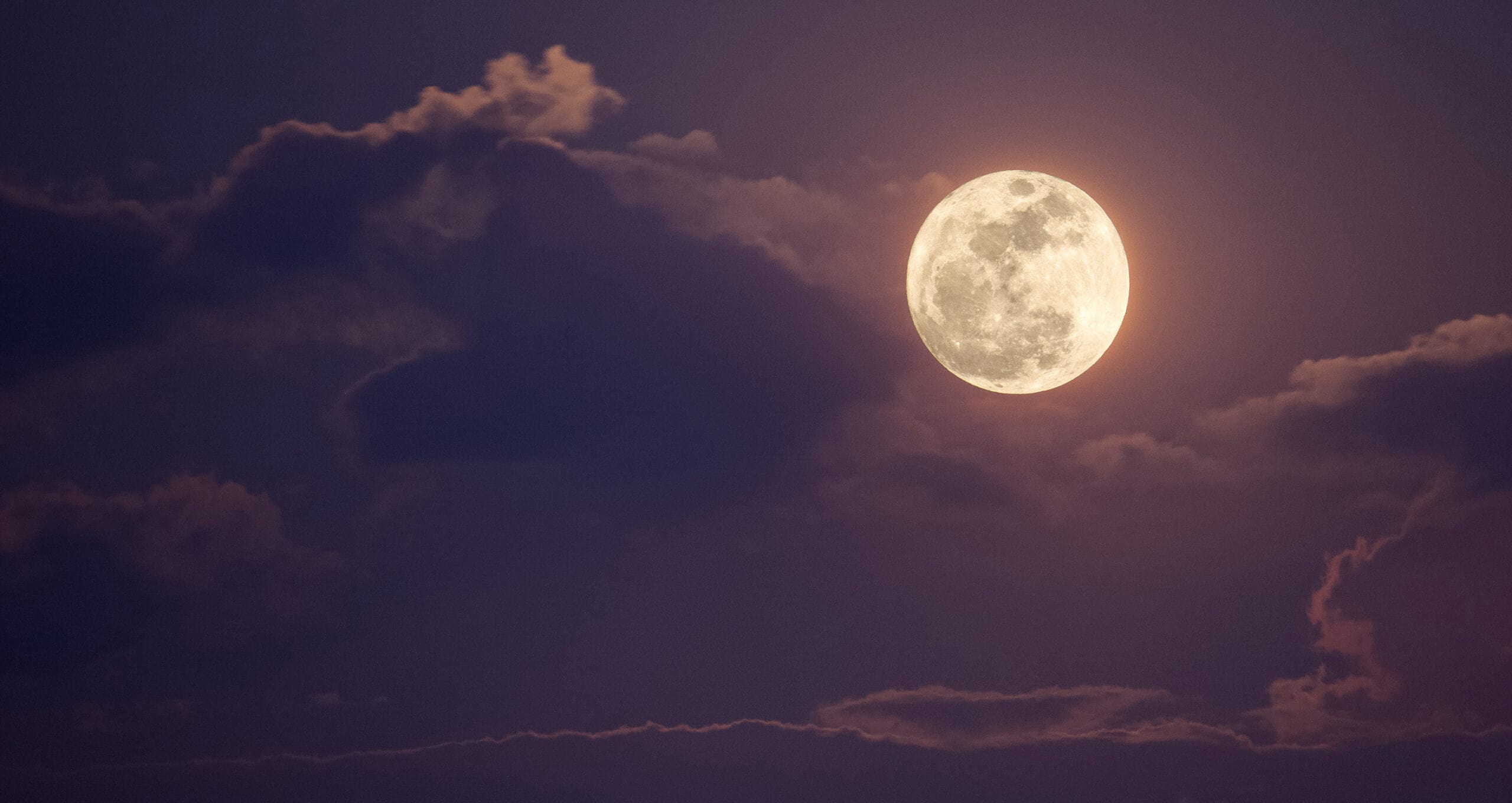 Full moon glowing behind clouds at night