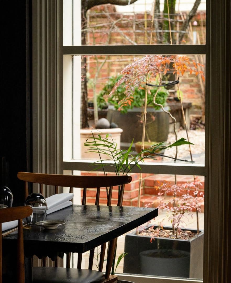 Intimate dining room at Kadota in Daylesford, with timber furniture and views through large windows to the garden.