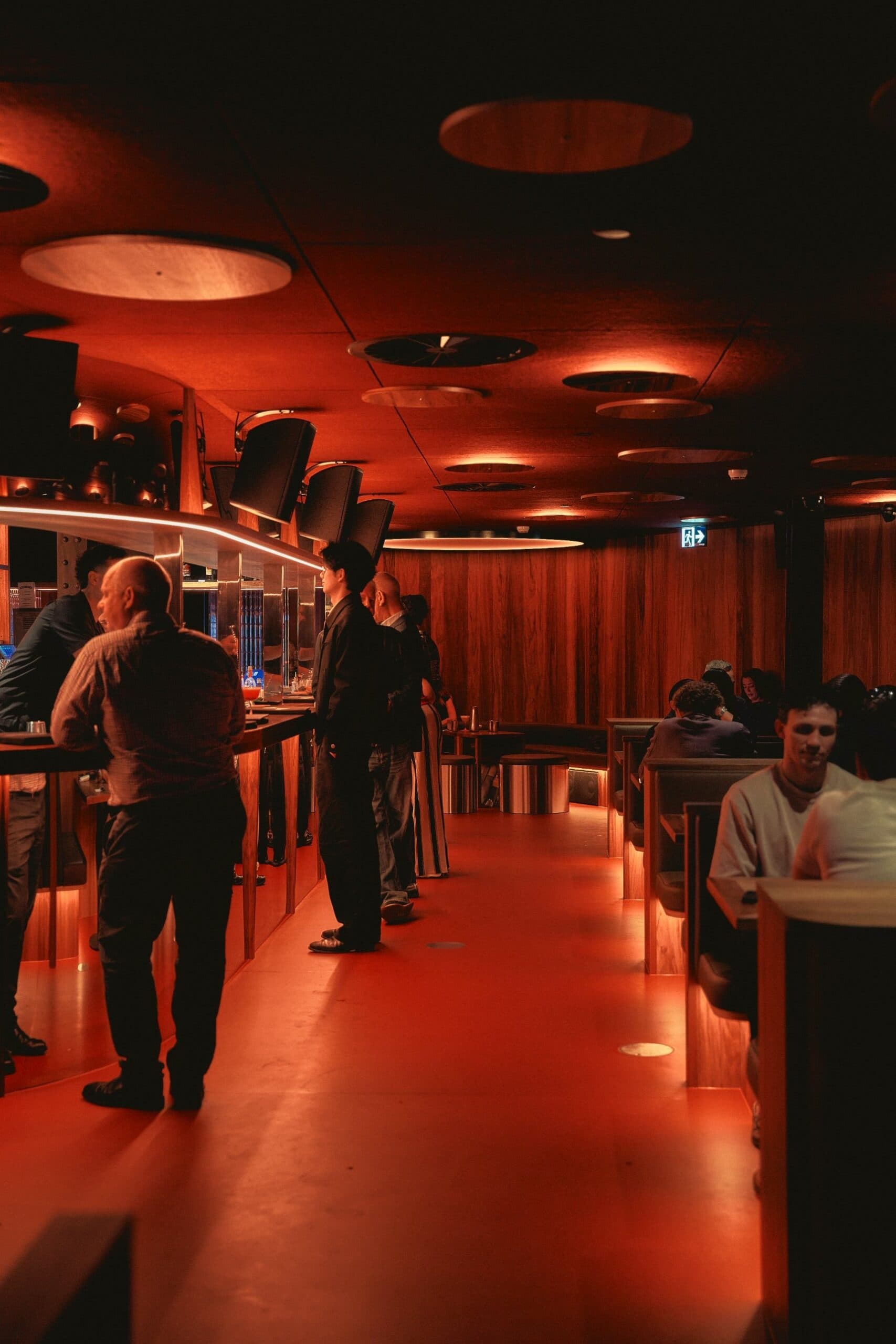 Red-lit interior of Loa late-night music bar on Oxford Street, with guests at the long bar and timber booth seating, Darlinghurst Sydney