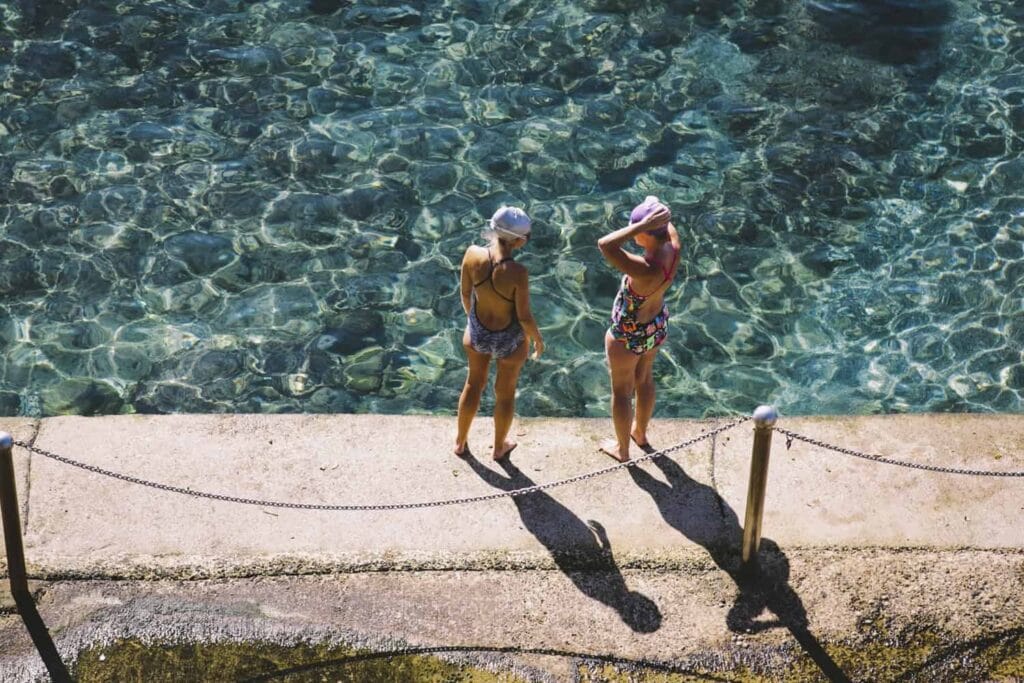 Two women in swim caps standing poolside at McIver Baths ocean pool, Coogee, Sydney