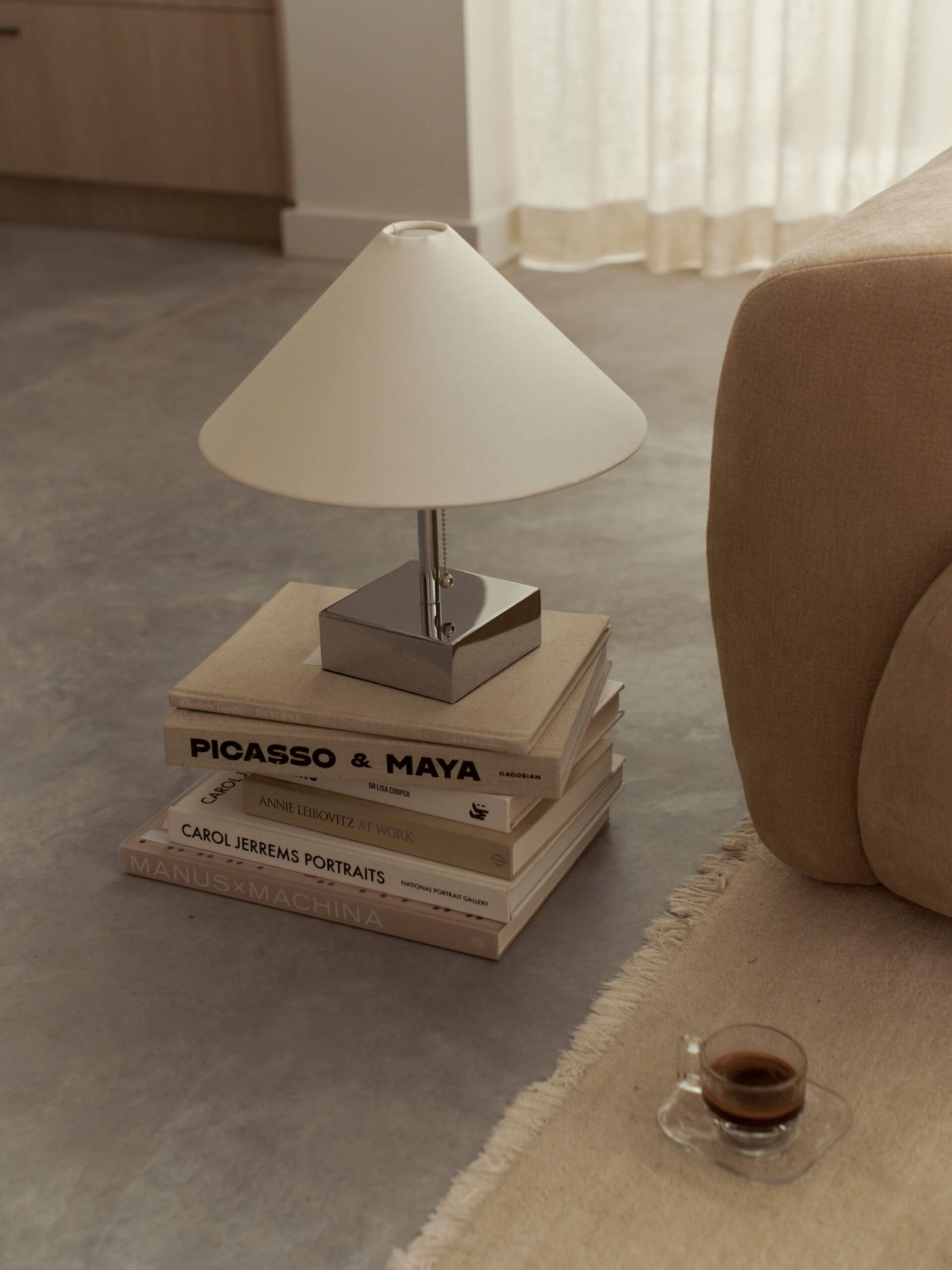 McMullin & Co table lamp on stacked art books beside sofa, espresso cup on rug