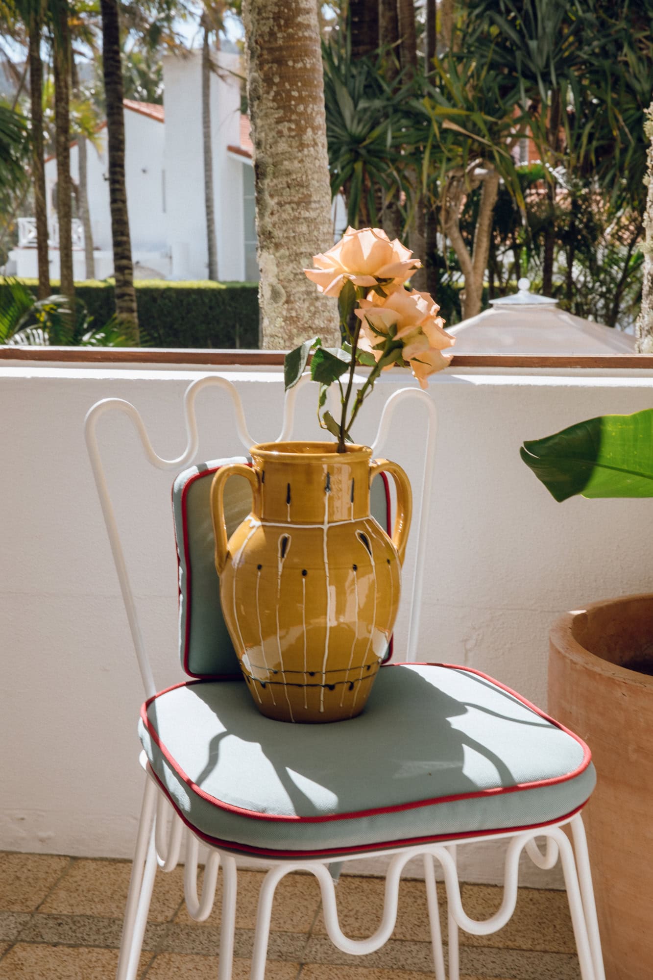 Honey Alex and Trahanas x Raes Antico vase with peach roses on a balcony chair at Raes on Wategos hotel, Byron Bay