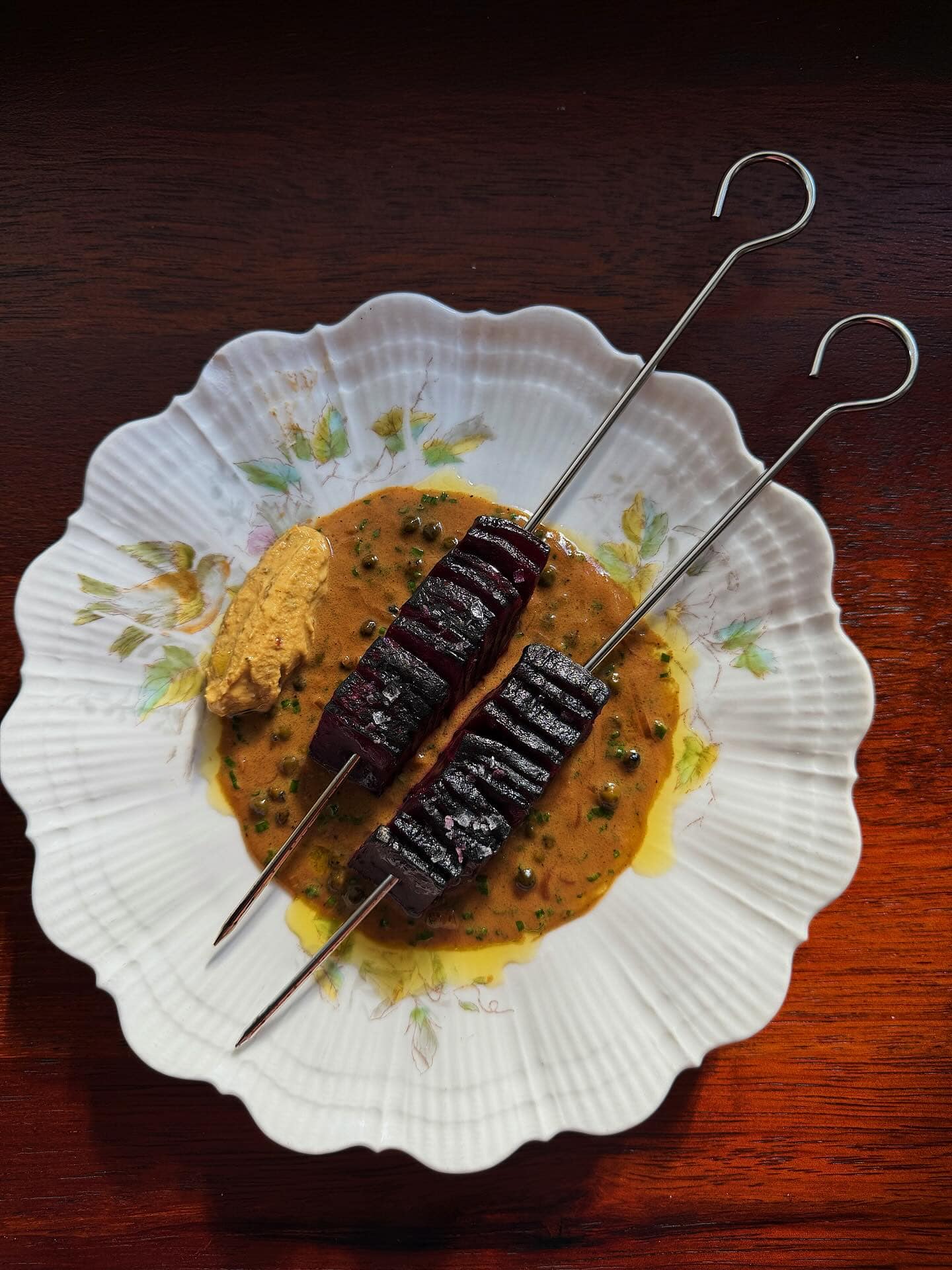 Two beetroot skewers served on a white ridged plate.
