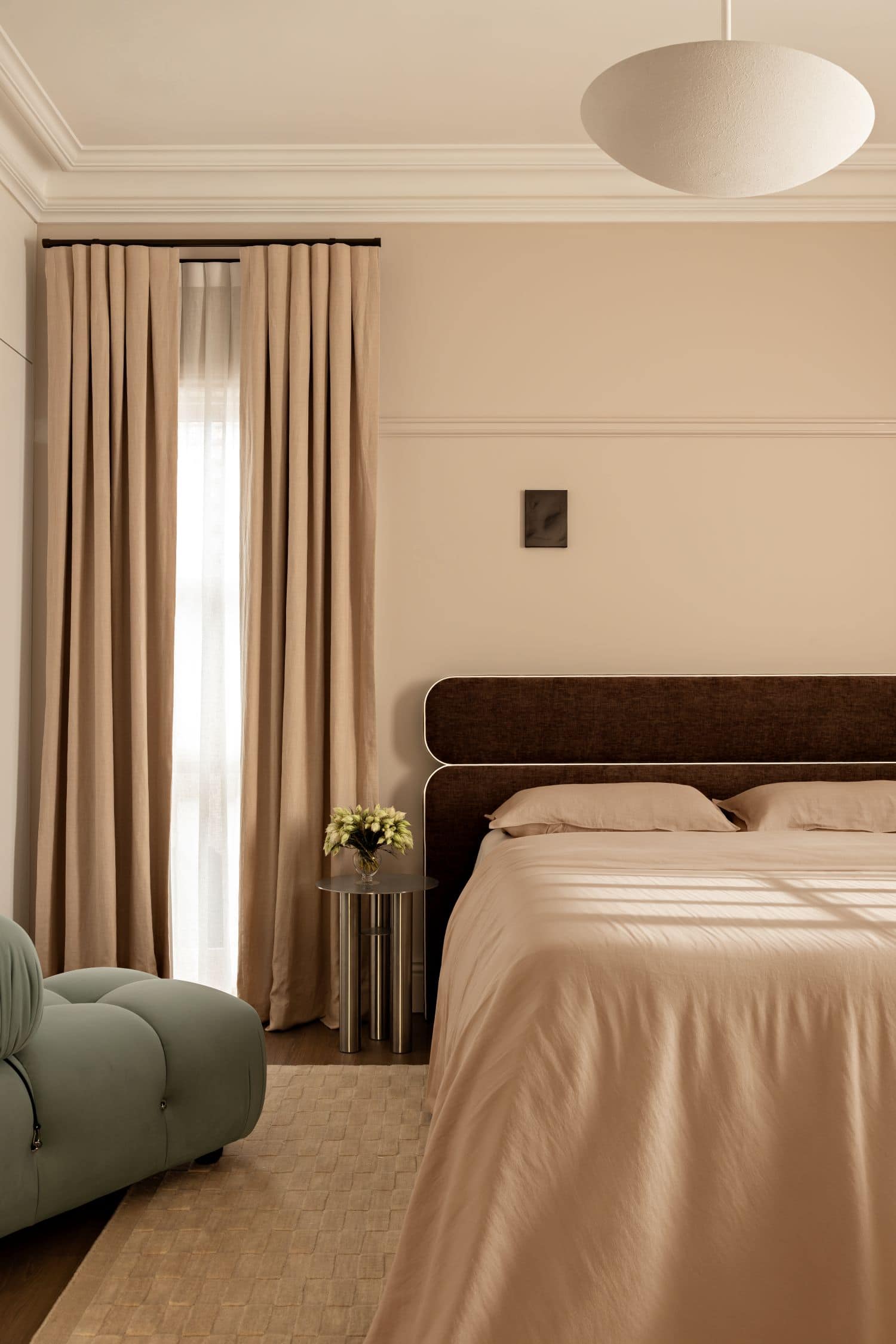 Bone Made x Beds Ahead Jean bed in brown suede made up with white sheets in a bedroom with flowers on side table and sage green occasional chair