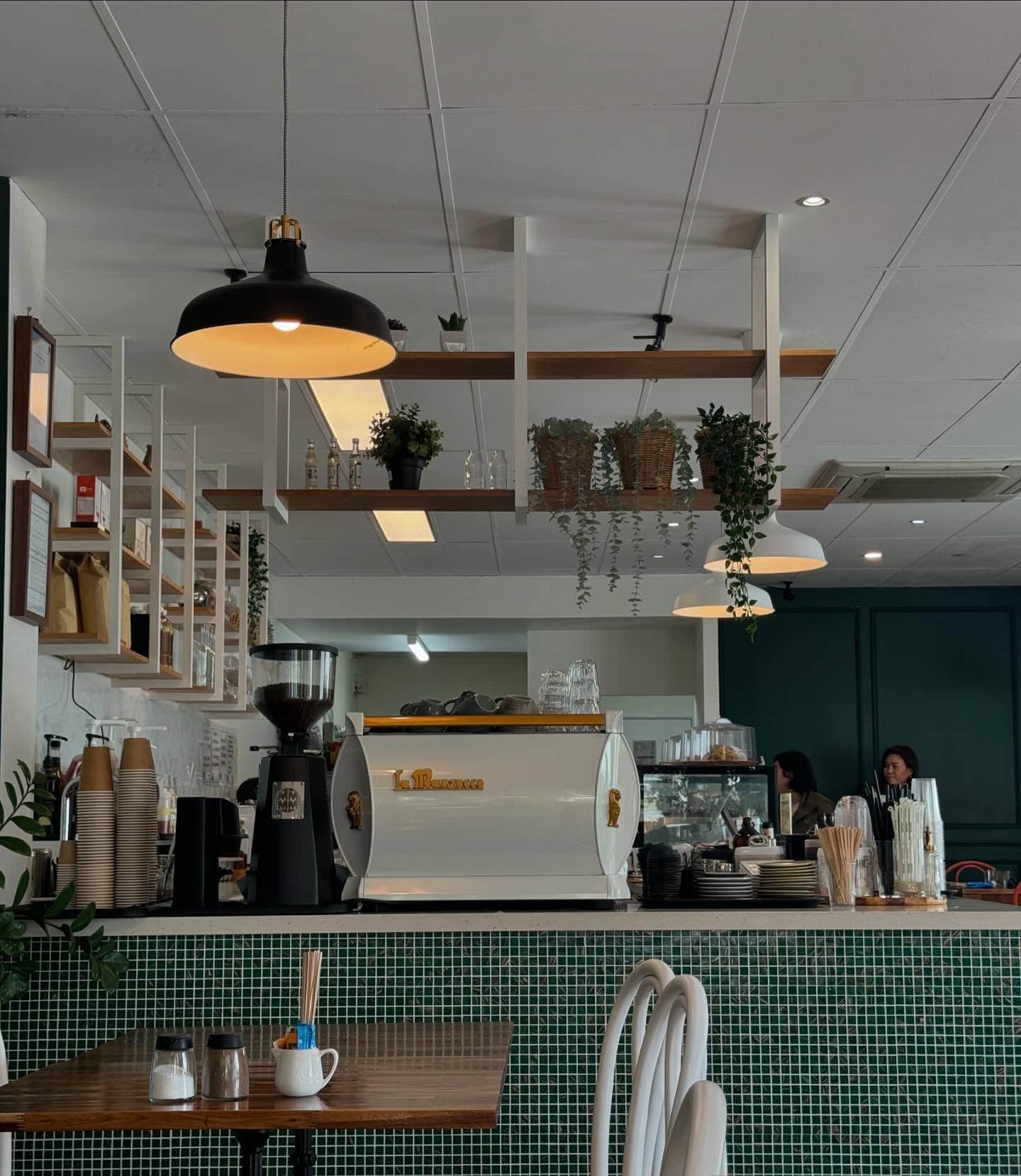 A coffee bar with small green tiles, a white coffee machine and servingware.