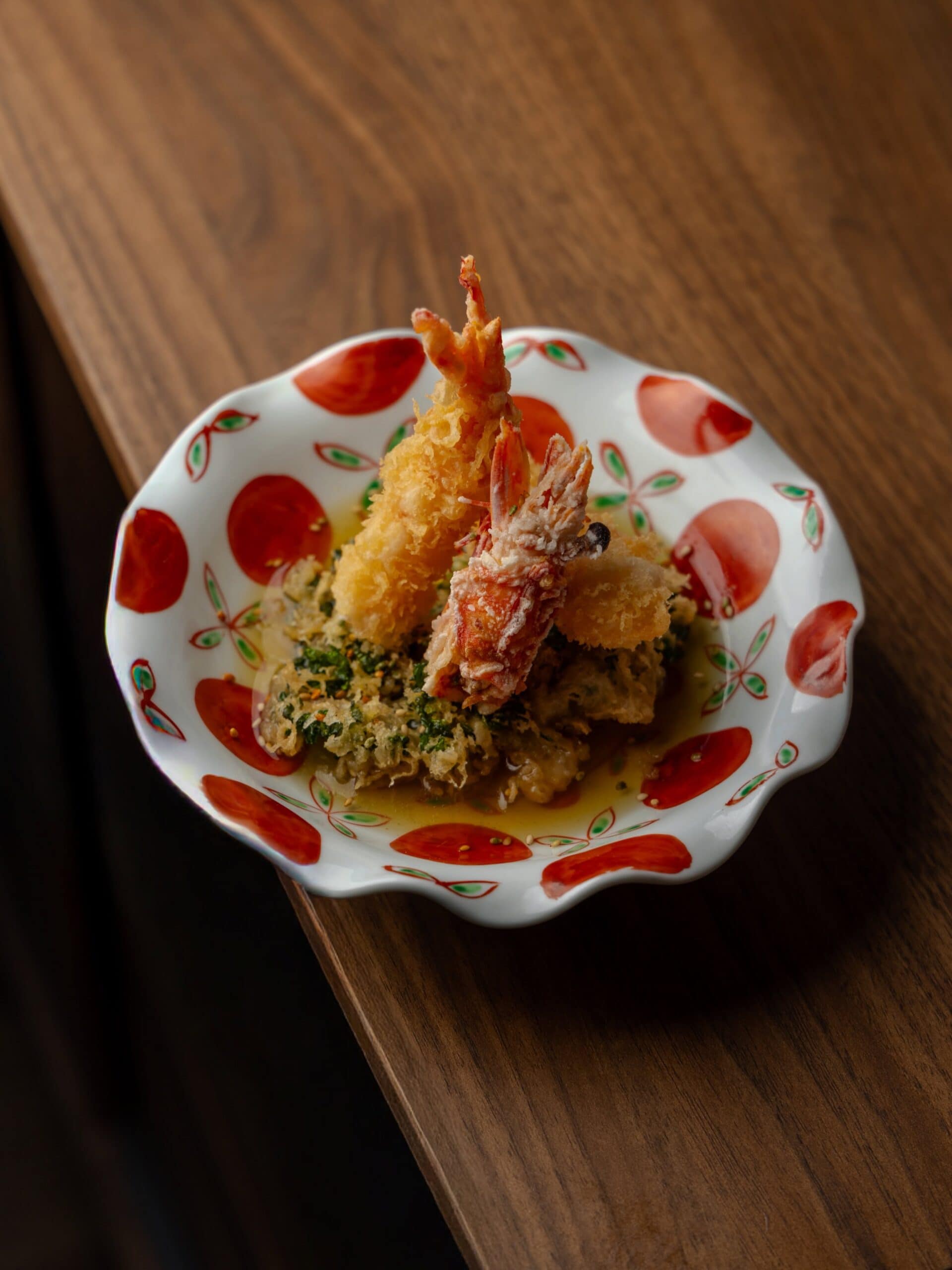 Two crumbed prawns served in a wavy red and white bowl on a brown table.