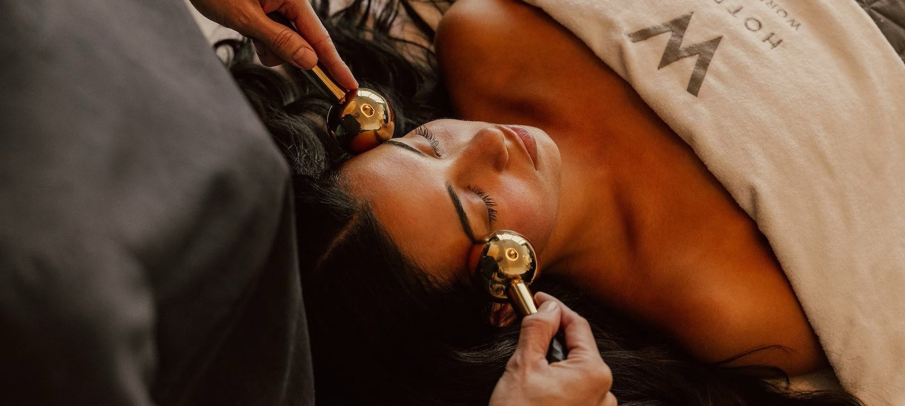 Top down view of a massage therapist using ice rollers on the face of their client on a massage table.