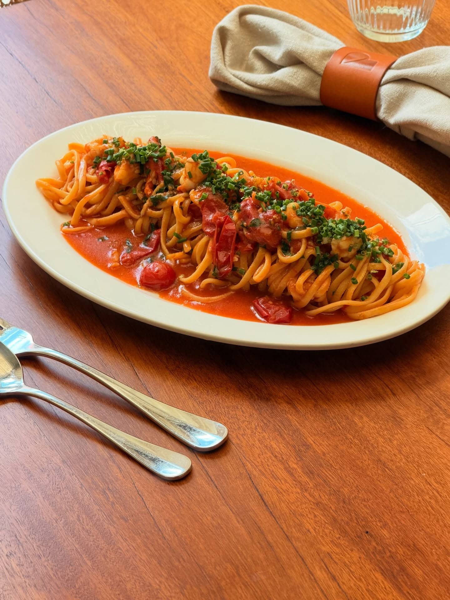 An oval plate with a share-sized serving of linguine in a light red sauce.