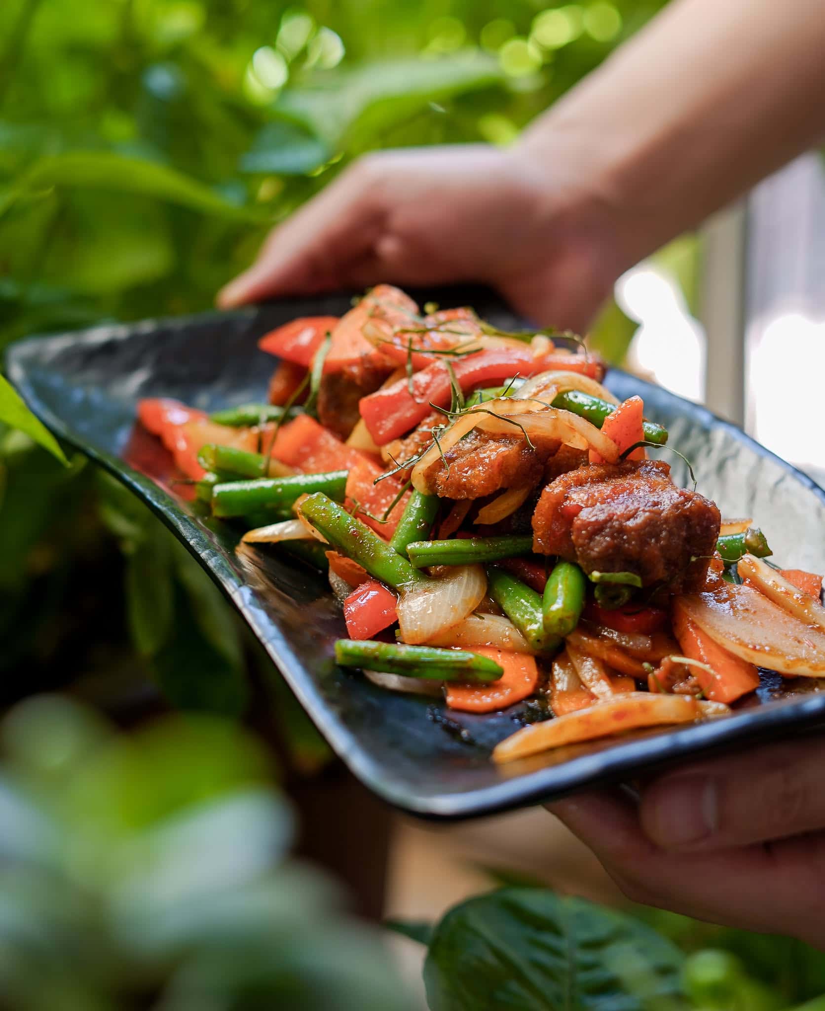 Two hands holding a black rectangular platter of crispy pork.