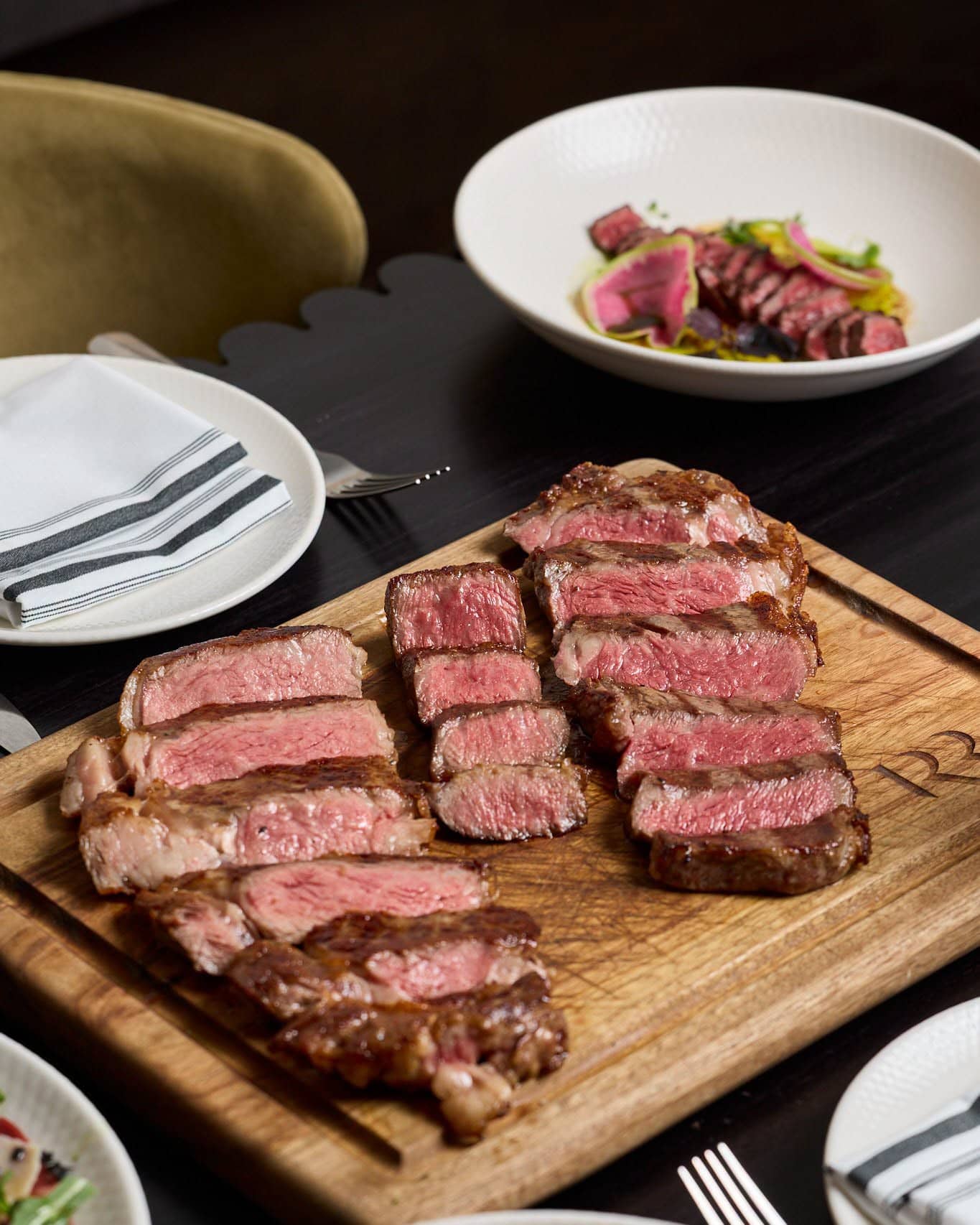 Three cuts of steak sliced on a wooden board.