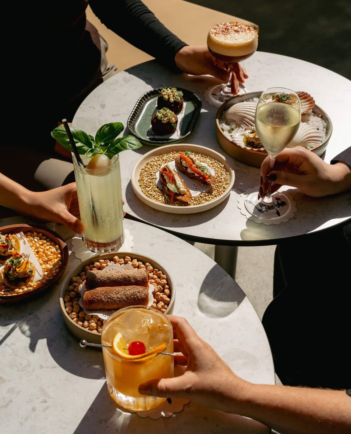 Five entree plates being shared among four people sitting outside with cocktails and sparkling wine.