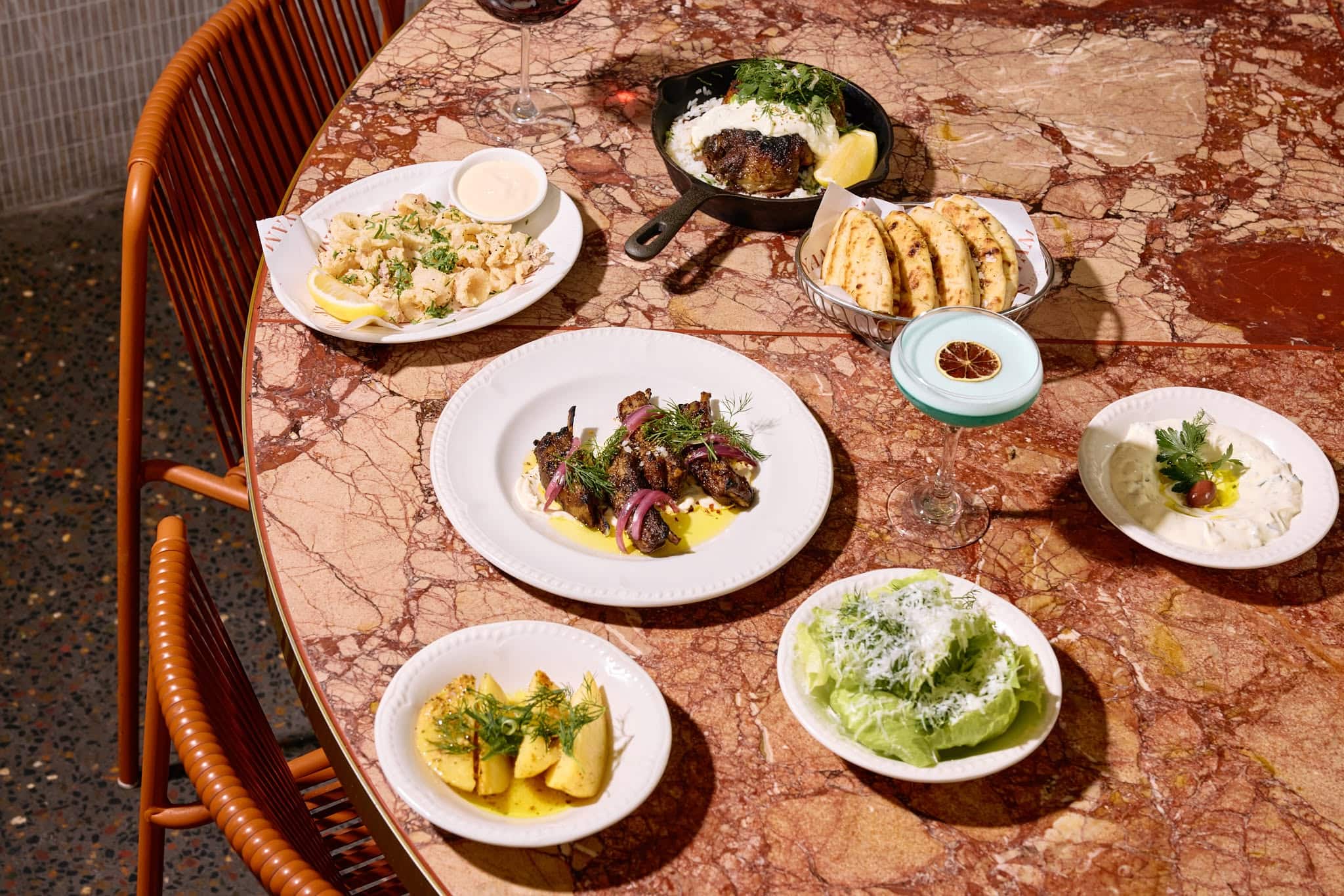 Calamari, salad, meats and tzatziki dip on a terracotta coloured marble table.
