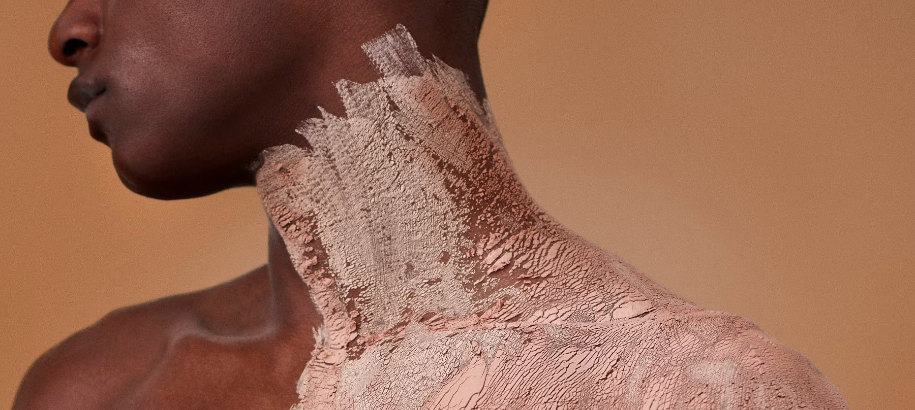 A close up shot of a pink clay skin mask on a person's neck, de colletage and shoulders.