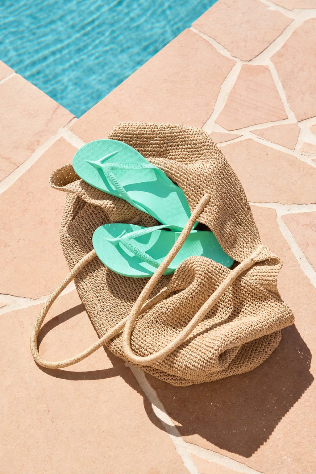 Mint Archies arch support thongs in a woven straw beach bag beside a pool