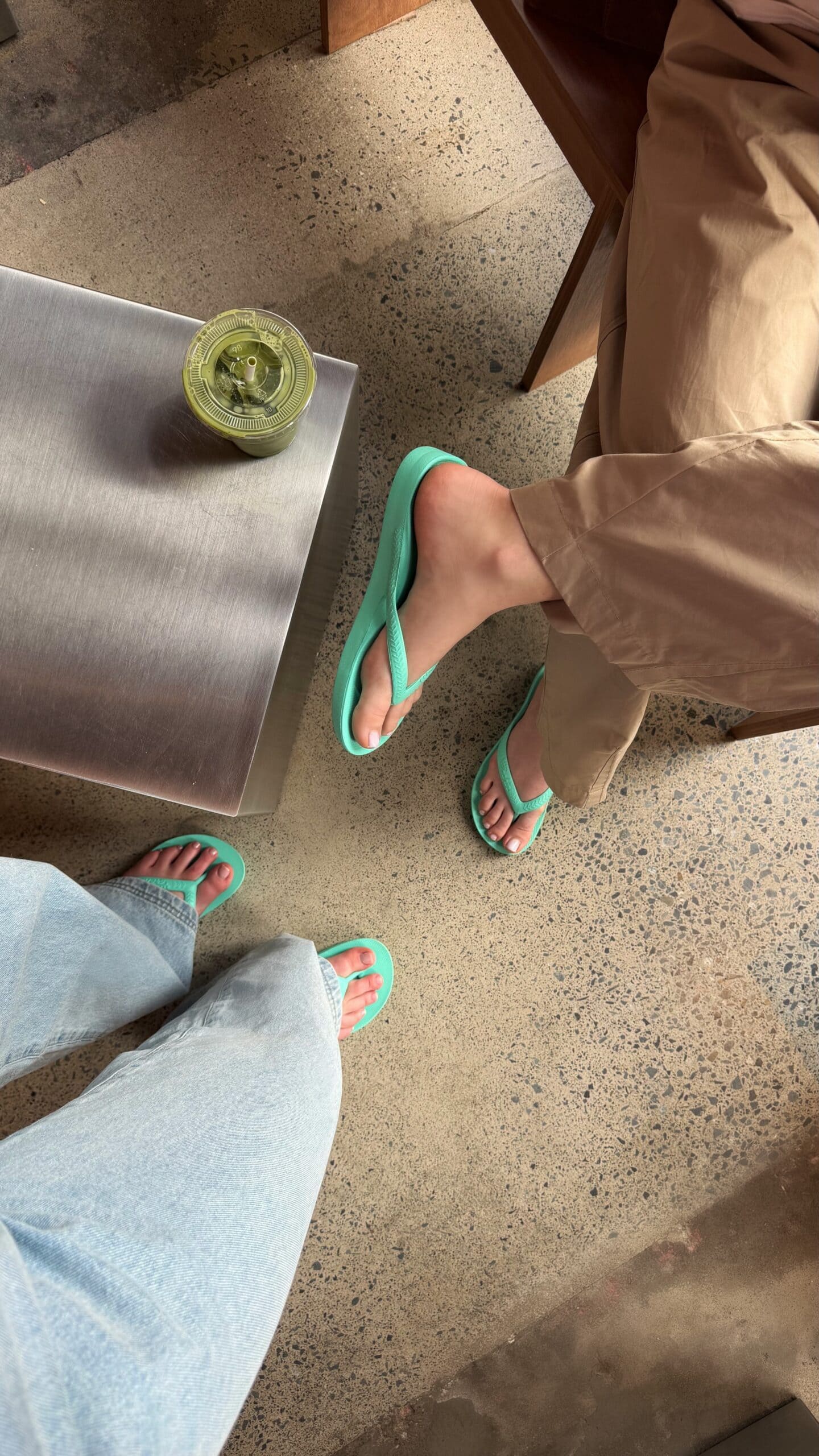 Two people wearing mint Archies arch support thongs beside an iced matcha, the thongs Archies is giving away free at Bondi Beach
