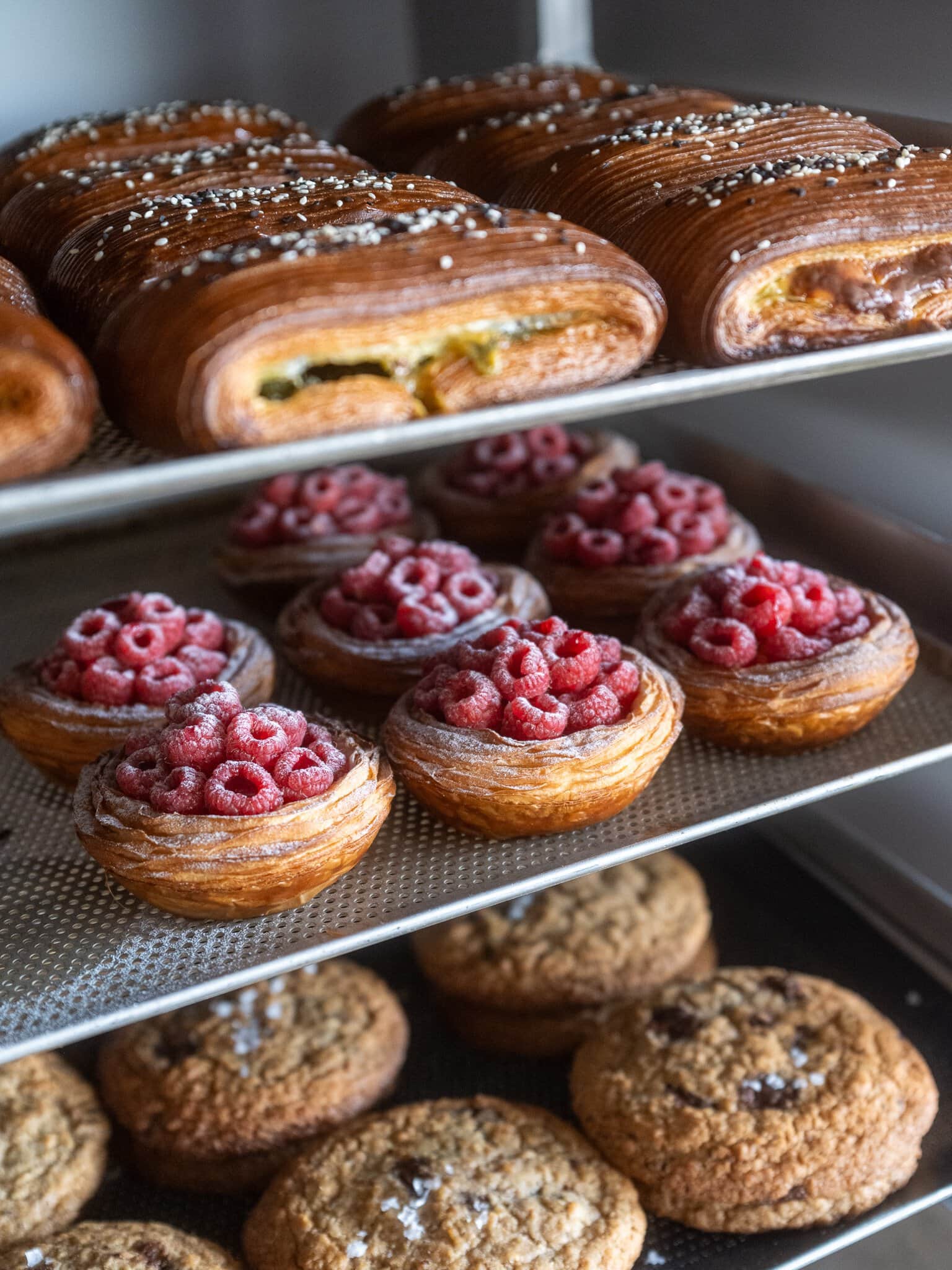 Trays of Popeye pain suisse with spinach and feta, fresh raspberry tarts and chocolate chip cookies at LoDe Pies & Pastries bakery, Sydney