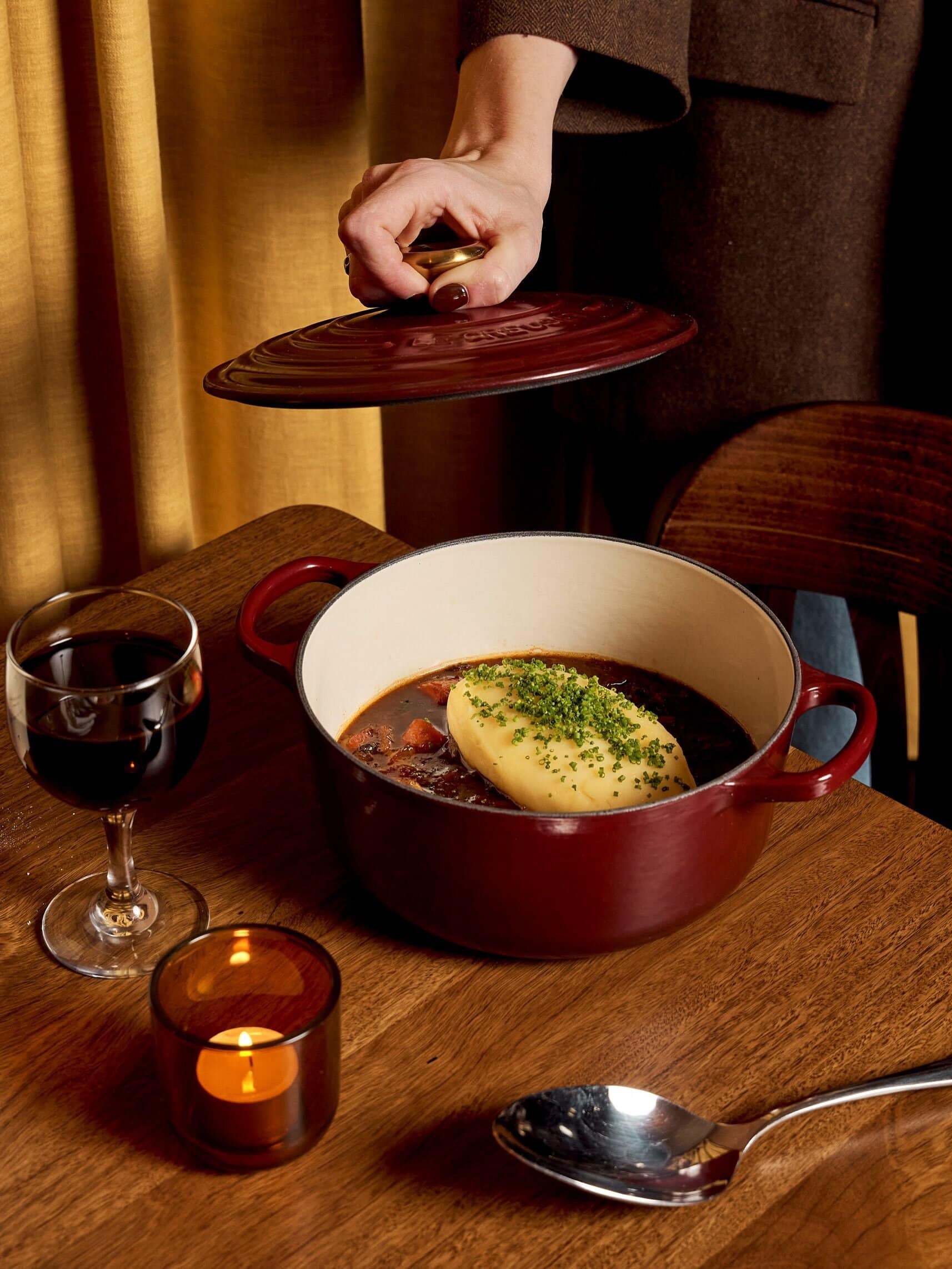 Boeuf bourguignon topped with chive-sprinkled mashed potato in a red cast-iron pot, served with red wine at Lucette French bistro, Bowral NSW