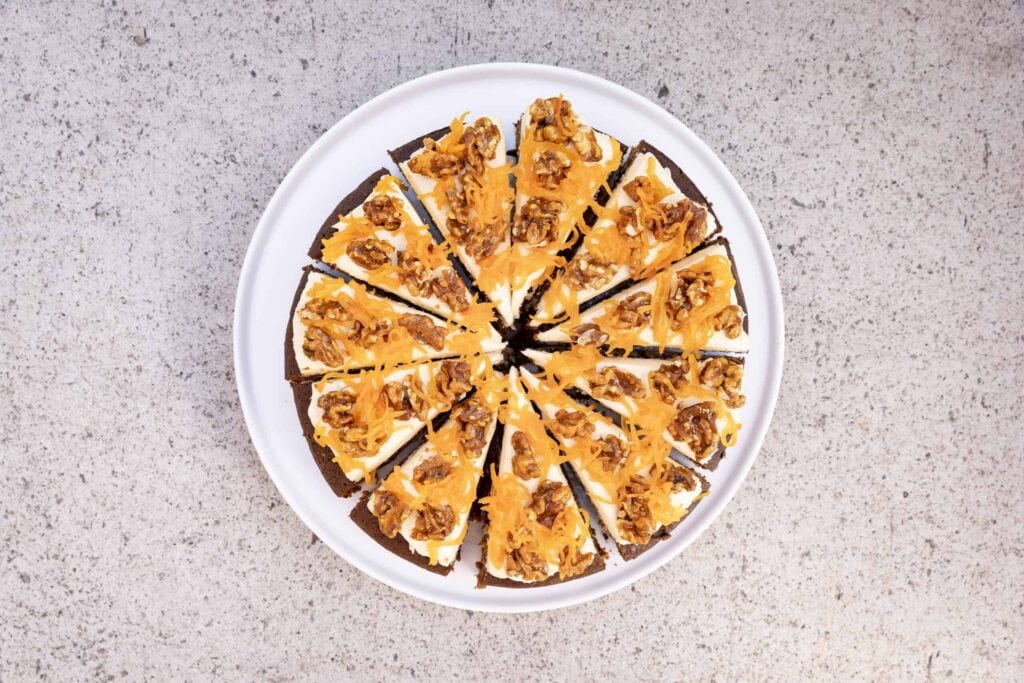 Sliced carrot cake with brown butter cheesecake frosting, candied walnuts and shredded carrot on a white plate, from Salma's Canteen, Rosebery Sydney