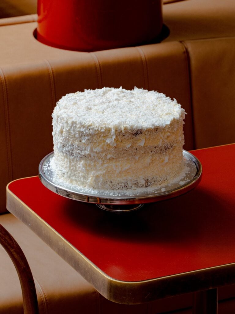 Coconut layer cake on a silver cake stand at Norma's Deli Manly Sydney