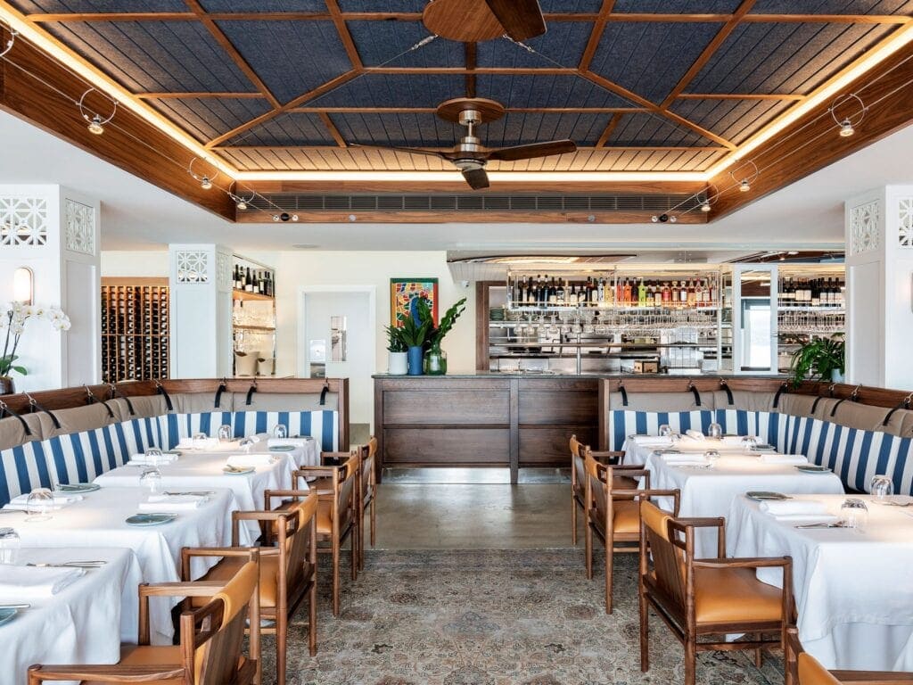 Dining room with blue and white striped banquettes and a timber ceiling at Bathers' Pavilion Restaurant, Balmoral Mosman Sydney, awarded two Hats in the Good Food Guide 2026