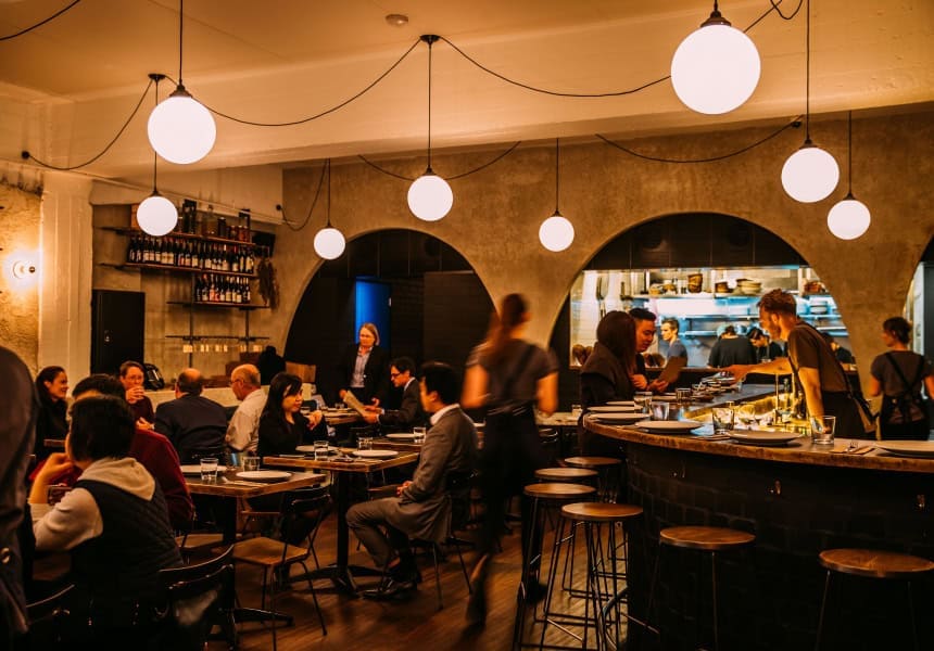 Dining room with concrete arches, globe pendant lights and an open kitchen bar at Ester, Chippendale Sydney, awarded two Hats in the Good Food Guide 2026