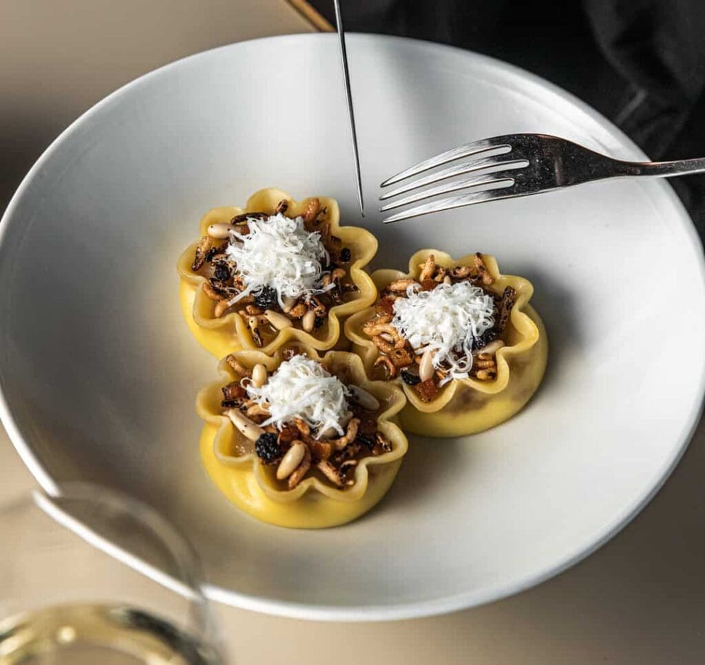 Filled pasta topped with pine nuts, currants, puffed grains and grated cheese at Bennelong, Sydney Opera House, awarded two Hats in the Good Food Guide 2026