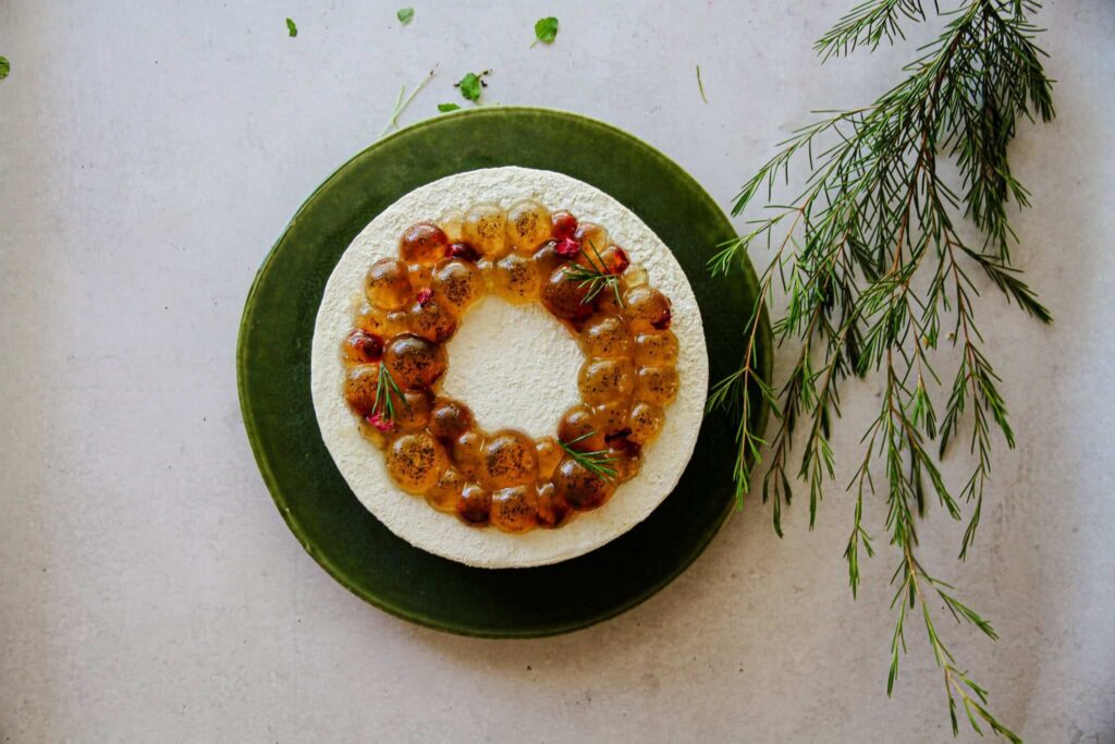 Geraldton wax cheesecake topped with a ring of native-infused jelly pearls and Geraldton wax sprigs on a green plate, at Hearthe cakery, Stanmore Sydney