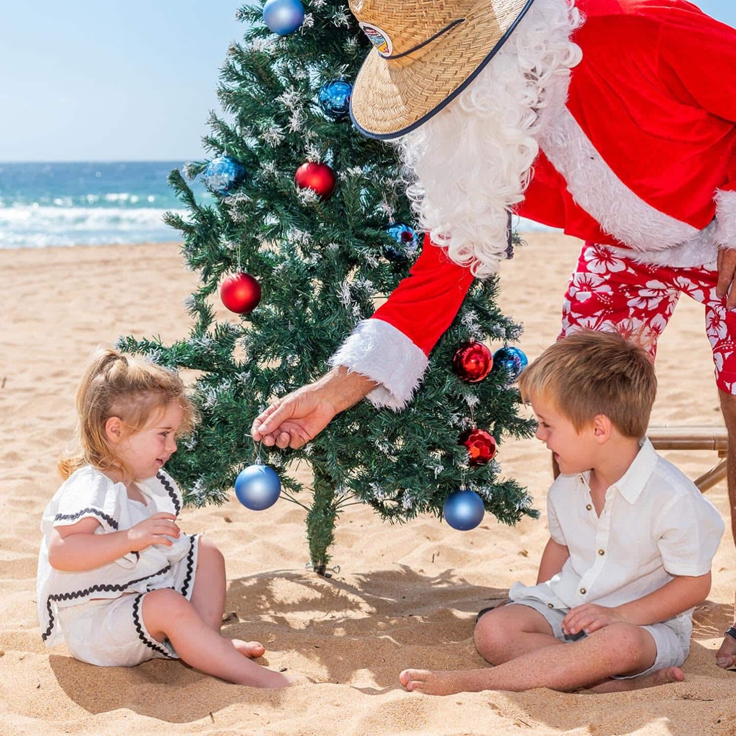 Santa handing a child a Christmas bauble on the beach