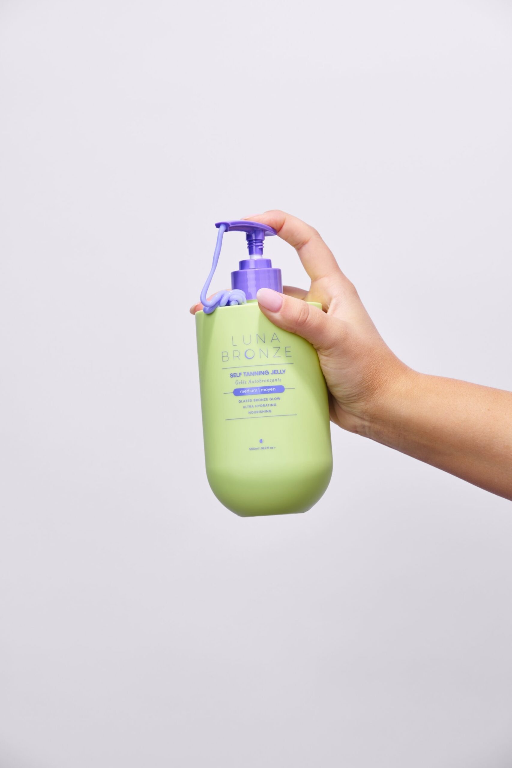 Hand holding Luna Bronze Self Tanning Jelly Jumbo 500mL bottle with purple jelly dripping from the pump