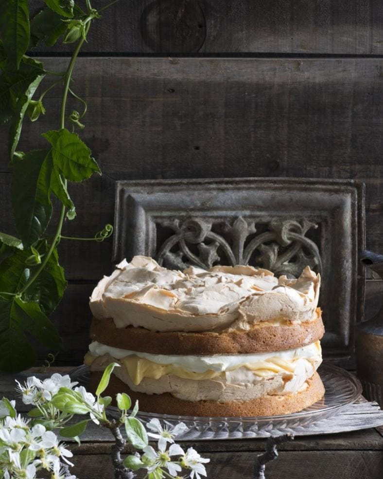 Layered sponge cake with meringue, whipped cream and custard on a glass stand, a special occasion cake by Flour and Stone bakery, Woolloomooloo Sydney