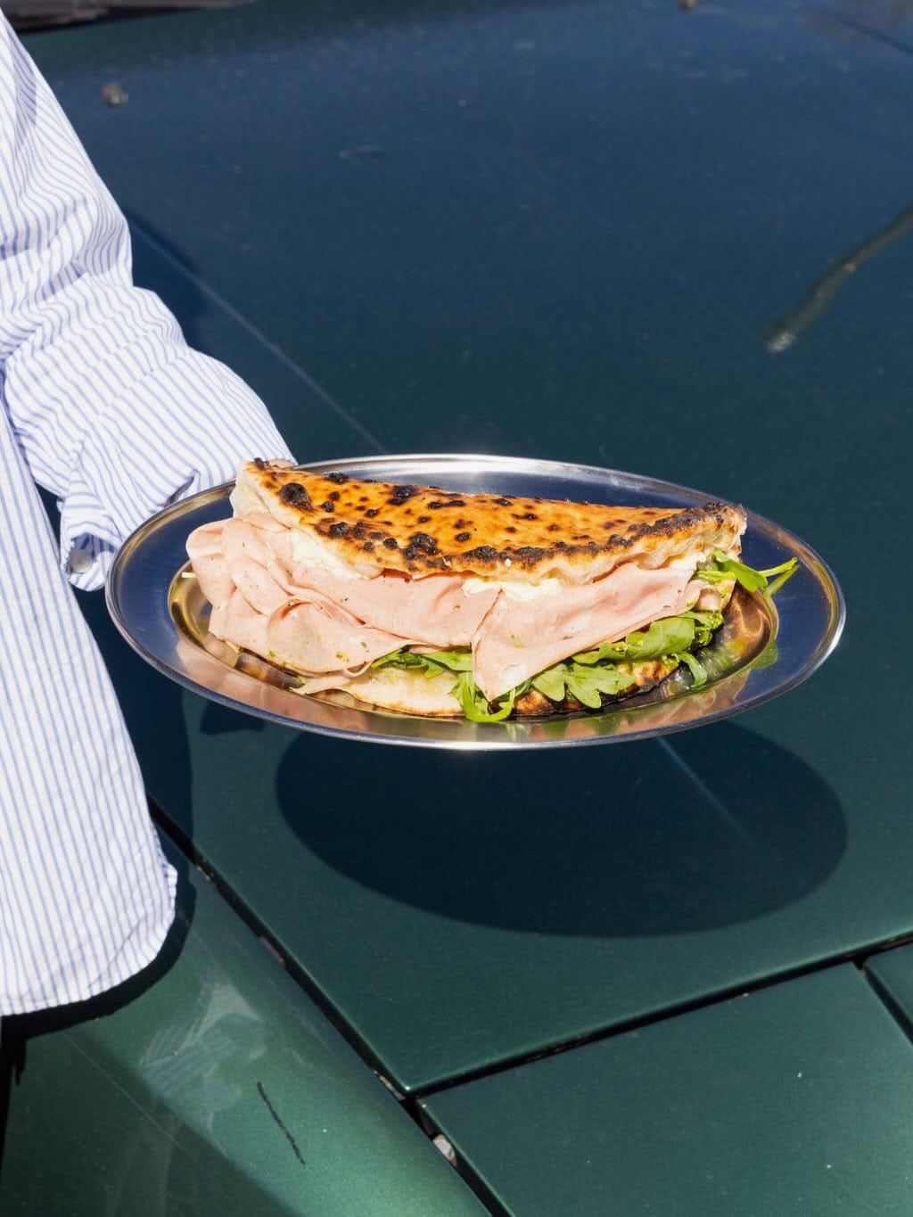 Wood-fired pizza bread sandwich filled with mortadella and rocket on a steel plate, from Pizzeria Officina's daytime sandwich menu, Braddon Canberra ACT
