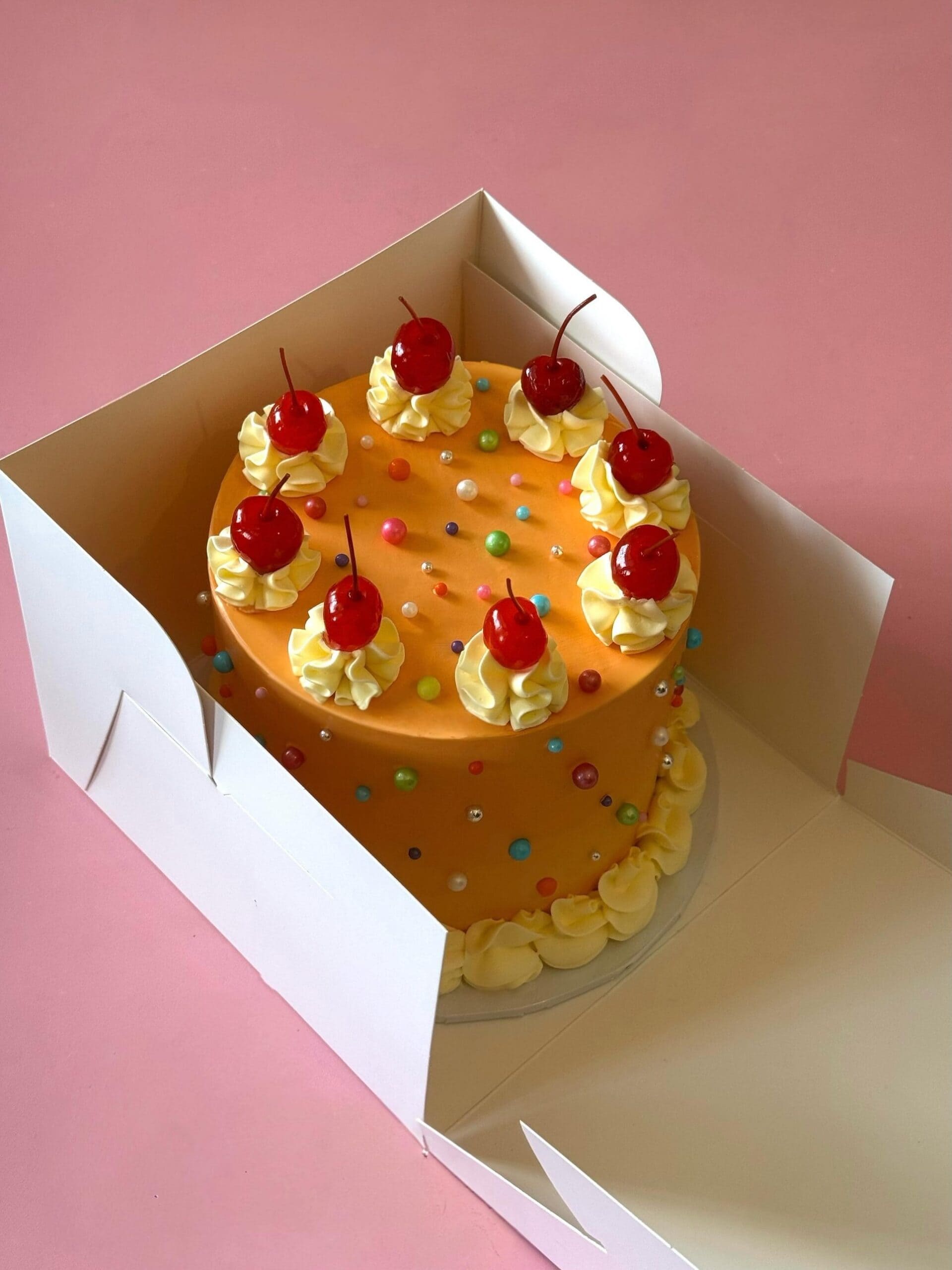 Retro orange buttercream custom cake with piped rosettes, glacé cherries and candy pearls in a cake box, by Javi Bakes, Rushcutters Bay Sydney