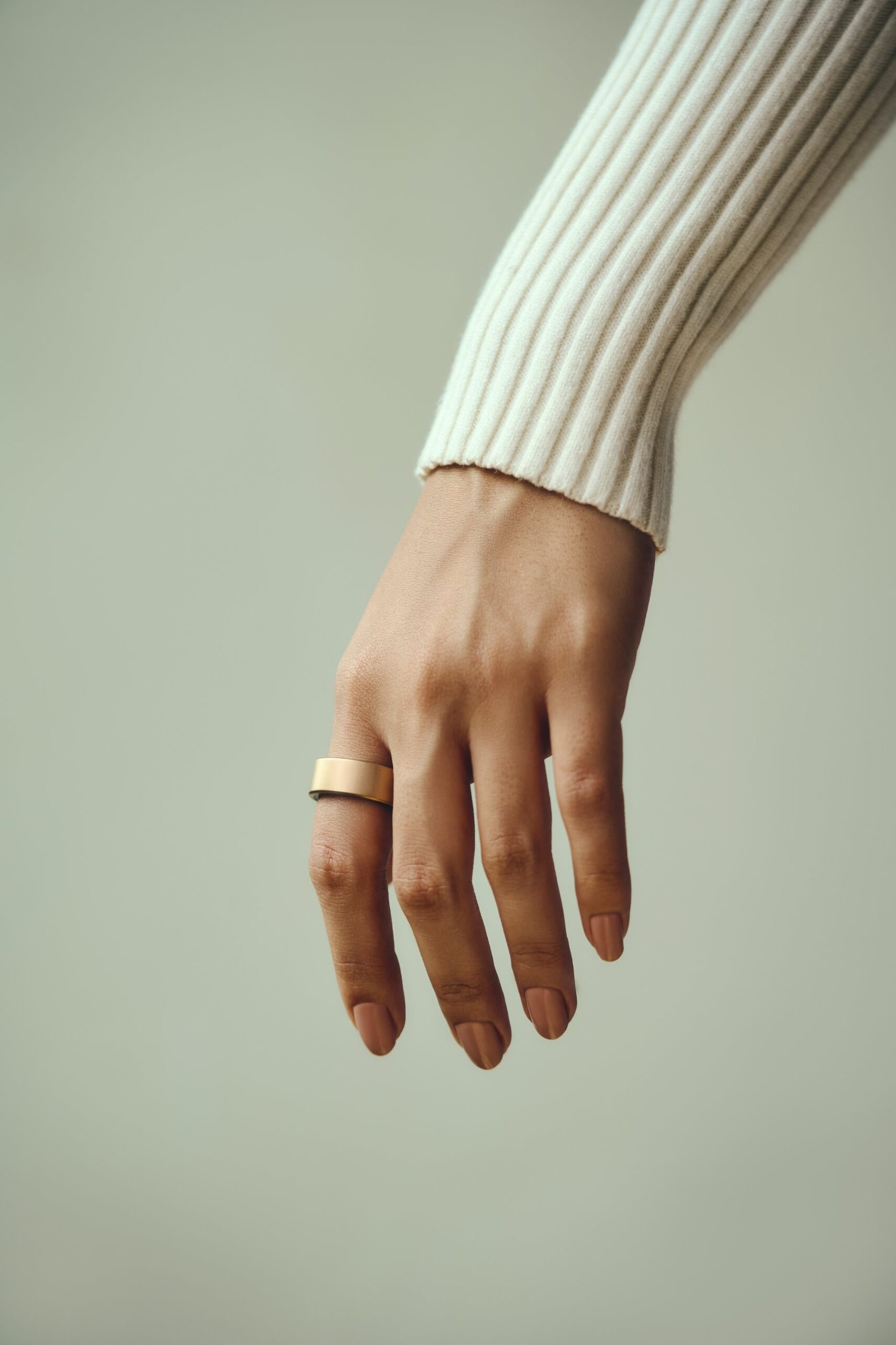 Hand wearing the Ultrahuman Ring AIR in Brushed Rose Gold with a cream ribbed sleeve
